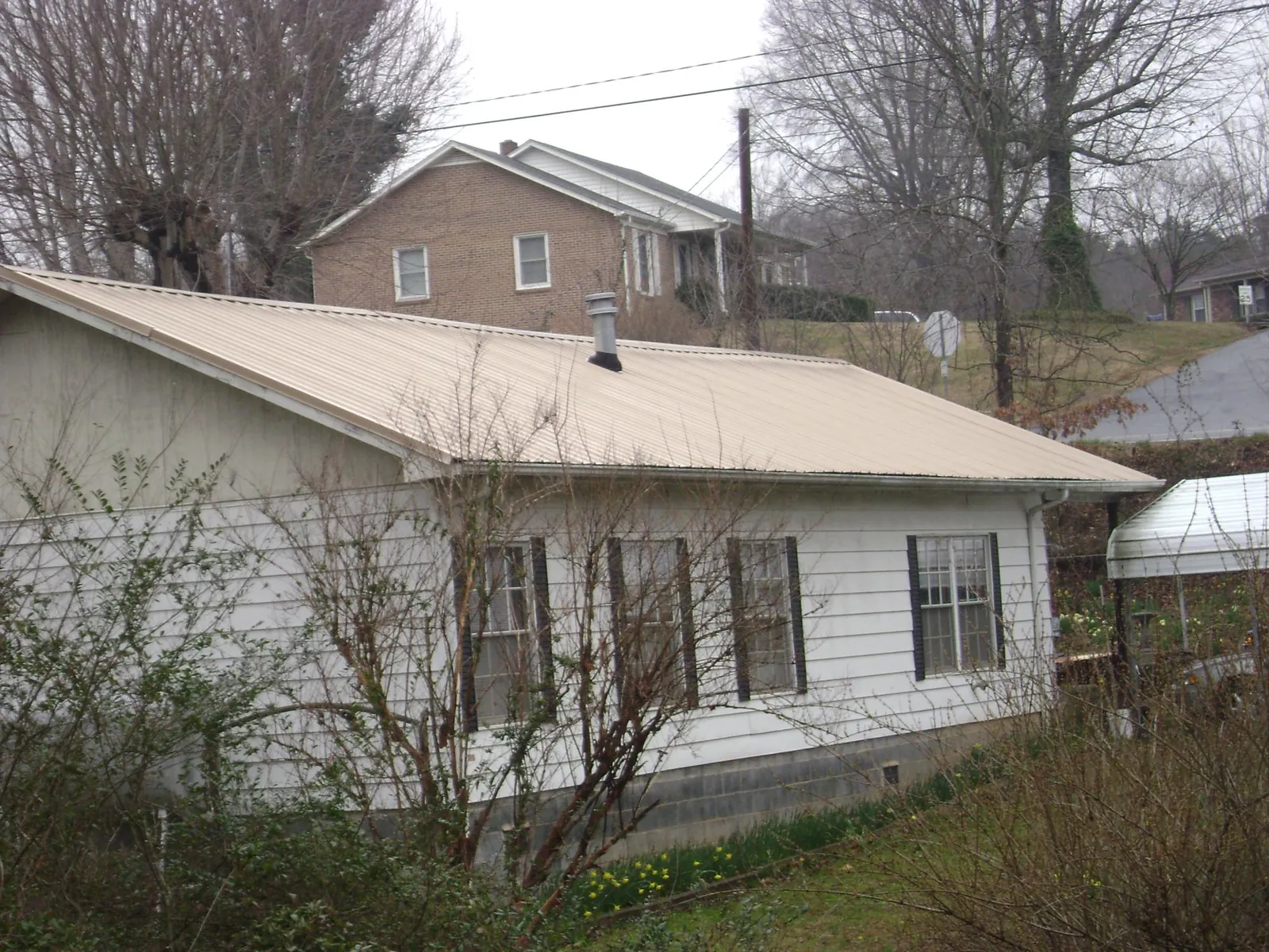 Tan metal roof on a white sided house set into a hillside in Avon
