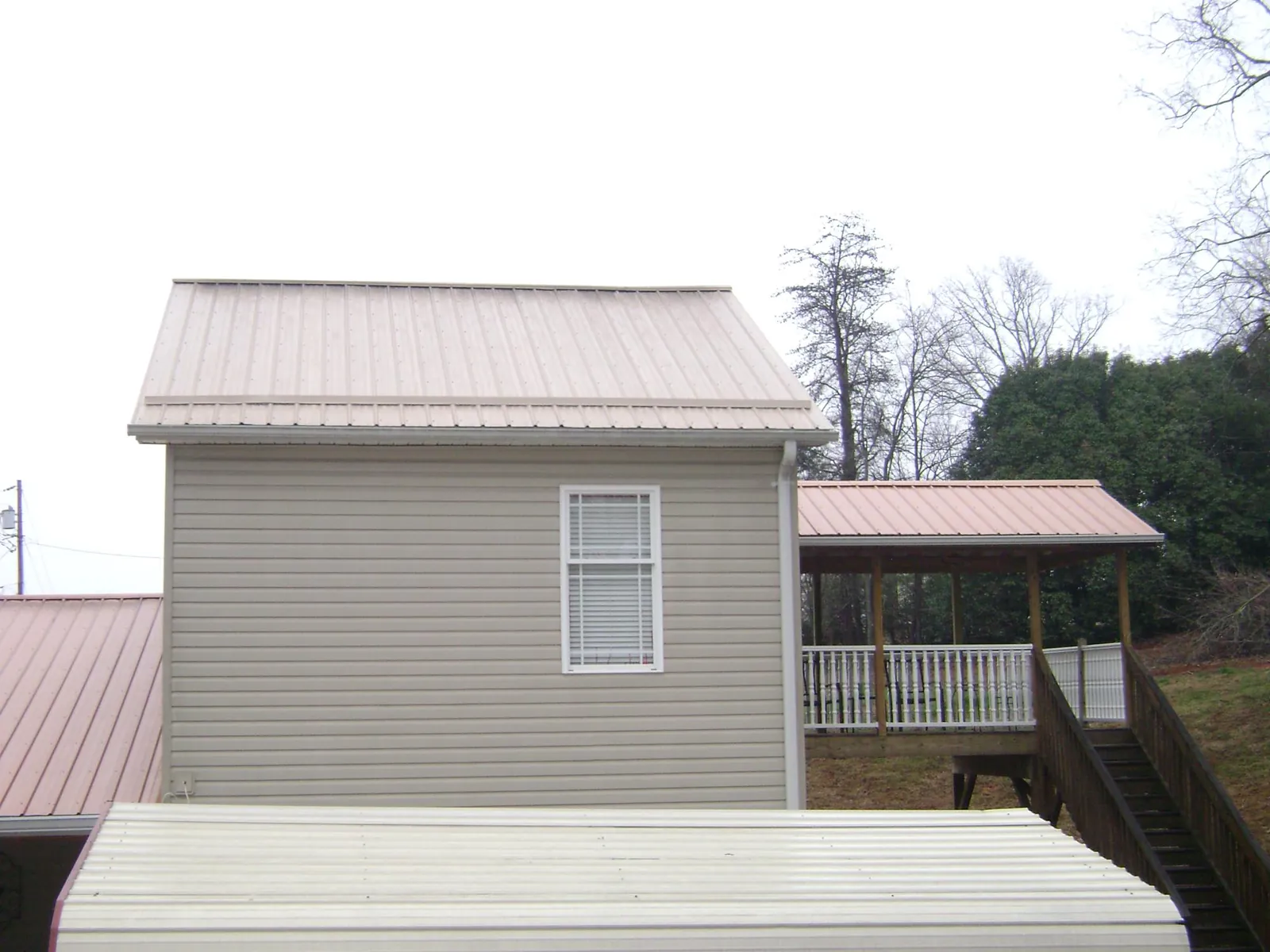Tan metal roofs on a two story addition and attached porch, from a Roof Replacement job in Avon